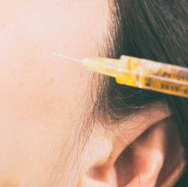 Syringe going into left side of a patient's face near their ear.